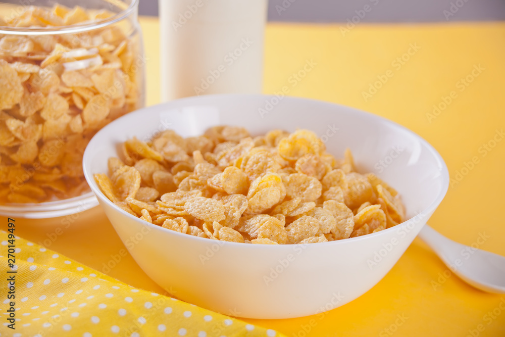 A bowl of dry corn flakes cereal on yellow background A bowl of dry corn flakes cereal on yellow background