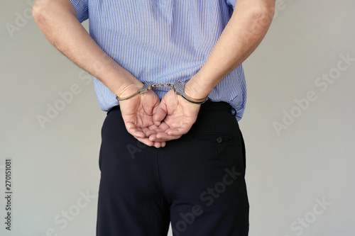 Arrested elderly man handcuffed hands at the back isolated on gray background. Prisoner or arrested terrorist, close-up of hands in handcuffs. Close-up view