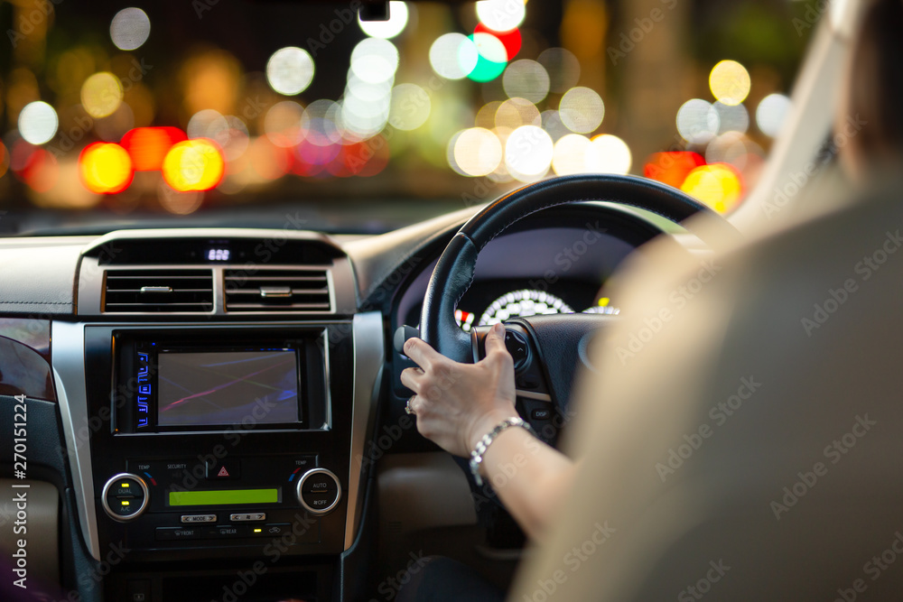 Woman driving a car with bokeh lights from traffic jam at night time.