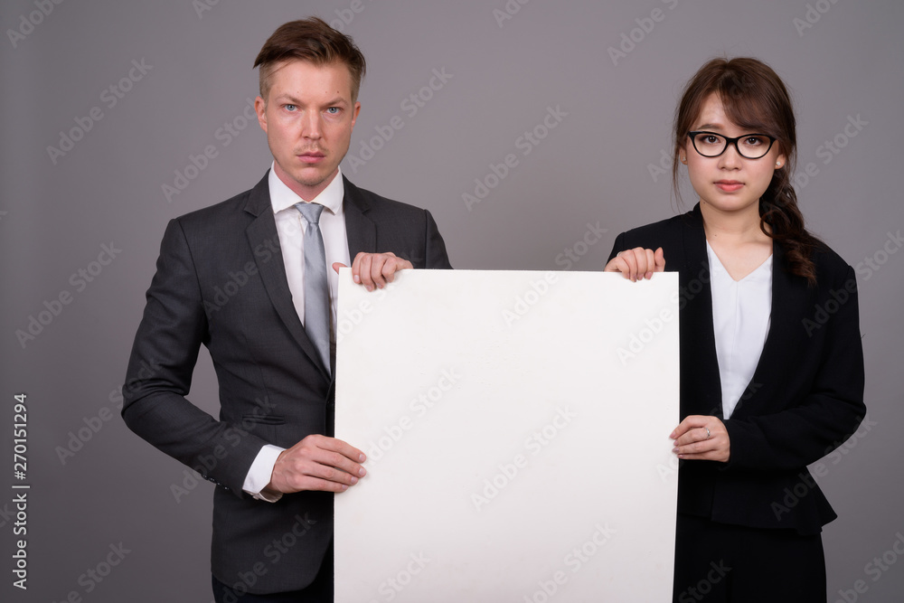 Young businessman and young Asian businesswoman against gray bac Young businessman and young Asian businesswoman against gray bac