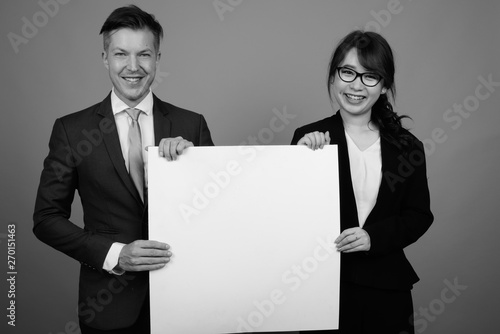 Young businessman and young Asian businesswoman against gray bac