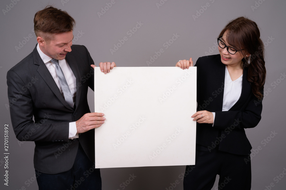 Young businessman and young Asian businesswoman against gray bac Young businessman and young Asian businesswoman against gray bac