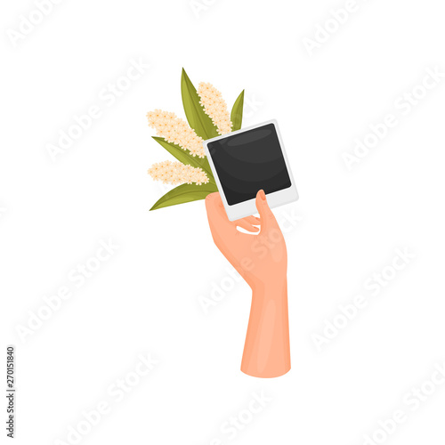 Hand holds a photo card of a poloroid and a bouquet of white inflorescences. Vector illustration on white background.