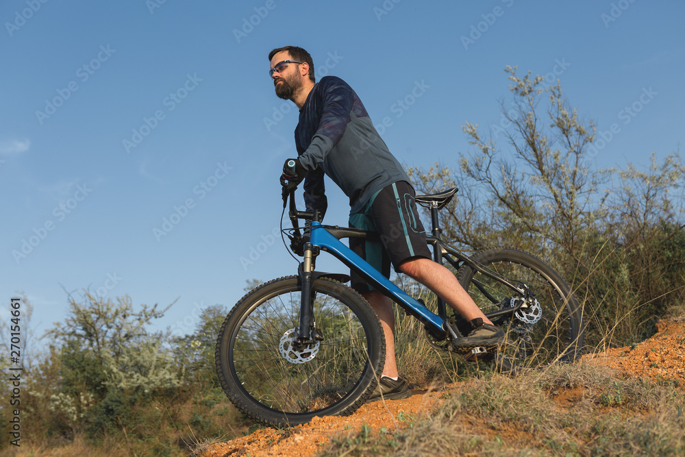 Obraz premium Cyclist in shorts and jersey on a modern carbon hardtail bike with an air suspension fork rides off-road on the orange-red hills at sunset evening in summer