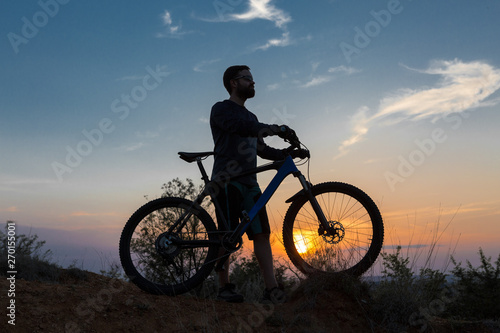Cyclist in shorts and jersey on a modern carbon hardtail bike with an air suspension fork rides off-road on the orange-red hills at sunset evening in summer © Mountains Hunter