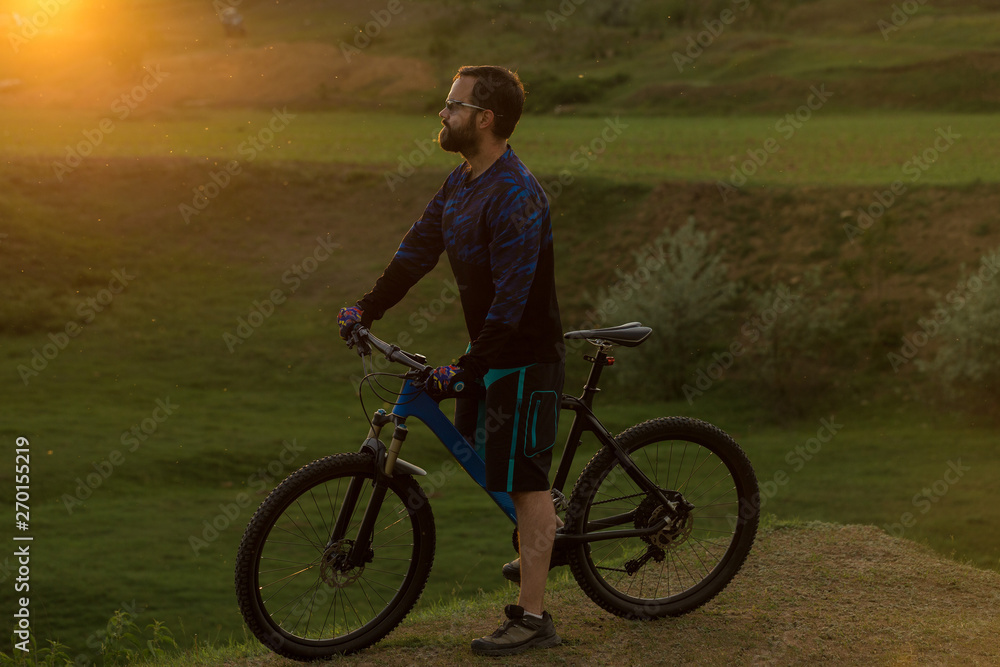 Cyclist in shorts and jersey on a modern carbon hardtail bike with an air suspension fork rides off-road on green hills near the forest Cyclist in shorts and jersey on a modern carbon hardtail bike with an air suspension fork rides off-road on green hills near the forest