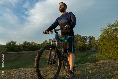 Cyclist in shorts and jersey on a modern carbon hardtail bike with an air suspension fork rides off-road on green hills near the forest  © Mountains Hunter
