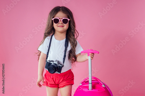 Portrait of little traveler girl on travel case with hat photo camera and passport ticet on pinc studio photo