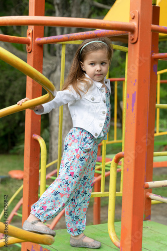 Little stylish blonde girl is having fun on a playground. Development of children in the open air in environmentally friendly conditions.