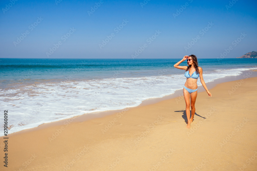 Young female imodel n a stylish blue bikini swimsuit enjoying sunny day on tropical beach paradise hotel resort.freedom and independence woman concept.copespase foam wave spf sunscreen