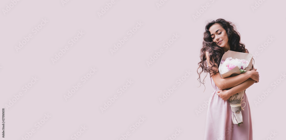 Young beautiful woman with long curly hair in a pink dress with a big bouquet of peonies on a pink background Young beautiful woman with long curly hair in a pink dress with a big bouquet of peonies on a pink background