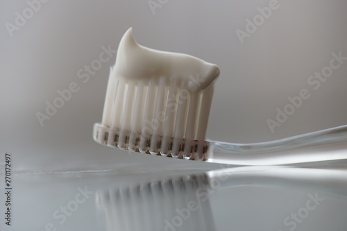Transparent plastic toothbrush with white toothpaste on a table with reflection on the glass.