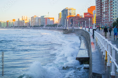 Waves splashing against the wall in San Lorenzo beach in Gijon, Asturias, Spain, with the promenade and buildings in one side photo