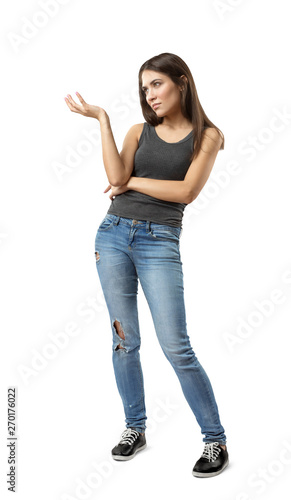 Young woman in gray sleeveless top and blue jeans standing with one hand bent and raised up, looking away, isolated on white background. photo