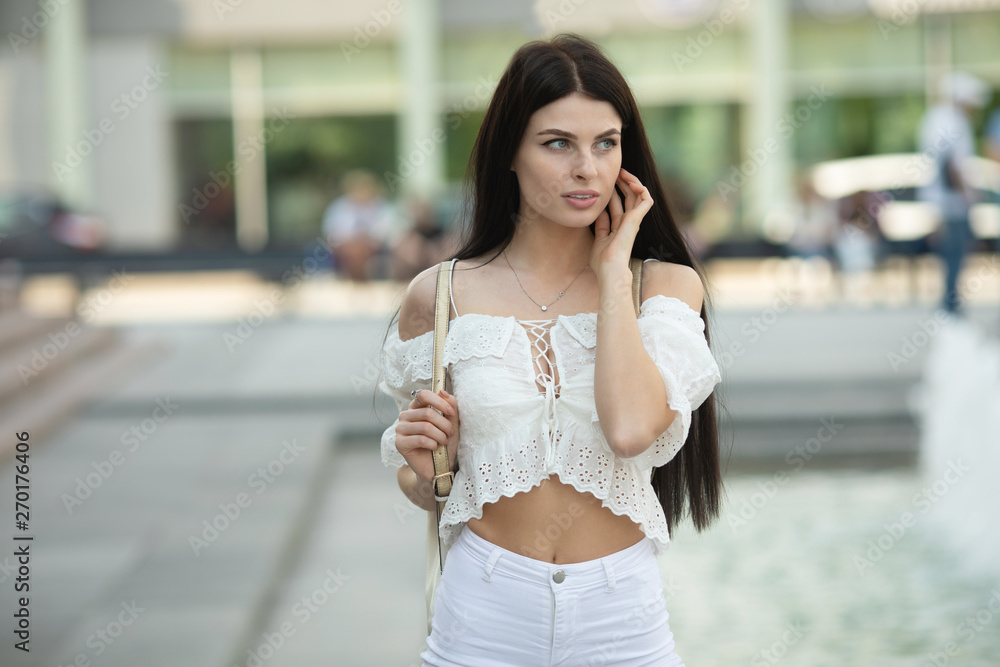 Outdoor fashion street stile portrait of pretty woman in casual outfit walking in city. Beautiful brunette girl or student enjoying weekends.
