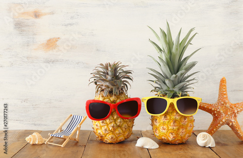 Ripe couple pineapple in stylish sunglasses over wooden table or deck, relaxing. Tropical summer vacation concept