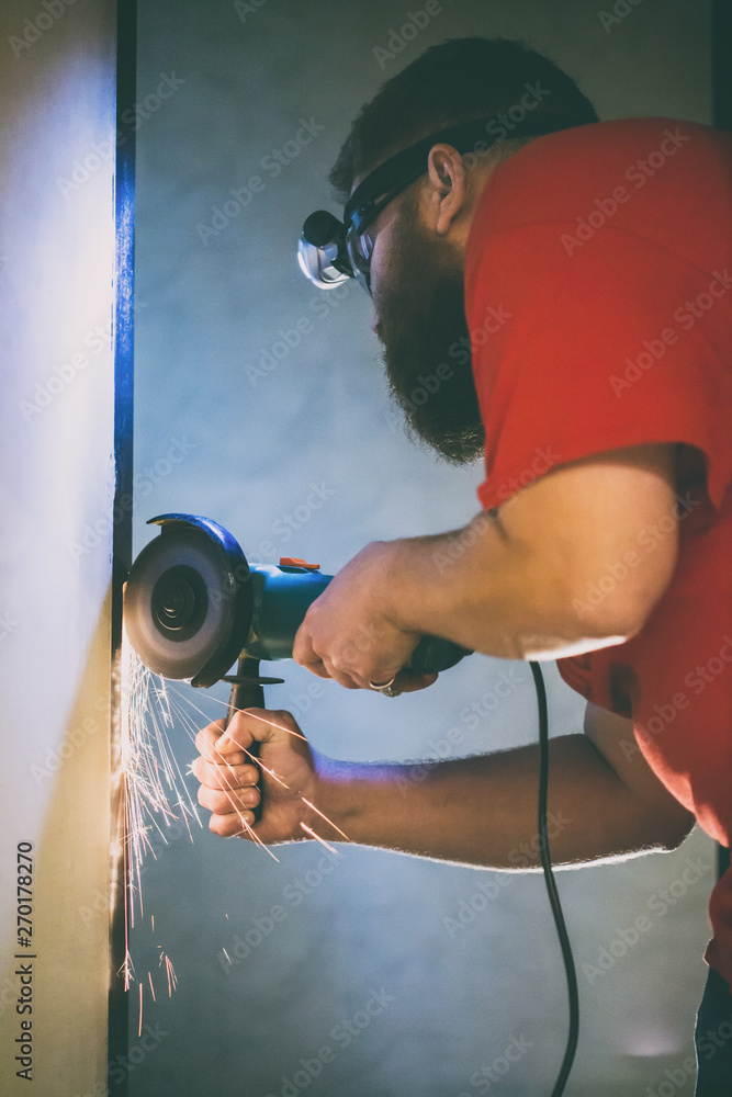 Naklejka premium A man repairs a door in the basement of his house using a manual grinding machine.