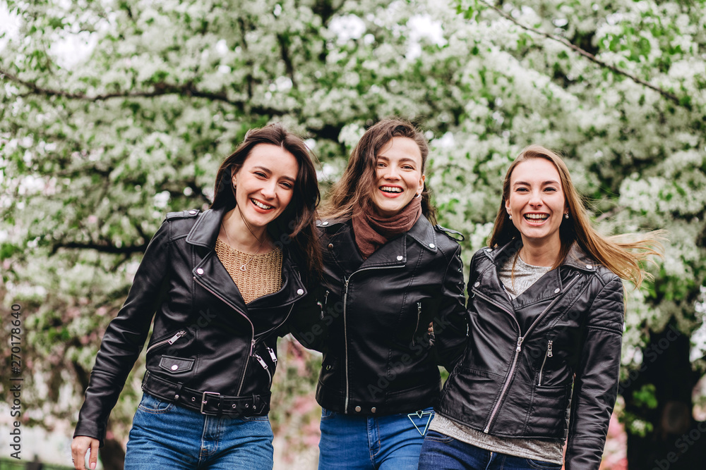 happy friends posing near blooming sakura flowers at cherry blossom trees during spring. Three young girls in leather jackets. Cute girl walks on nature. happy friends posing near blooming sakura flowers at cherry blossom trees during spring. Three young girls in leather jackets. Cute girl walks on nature.