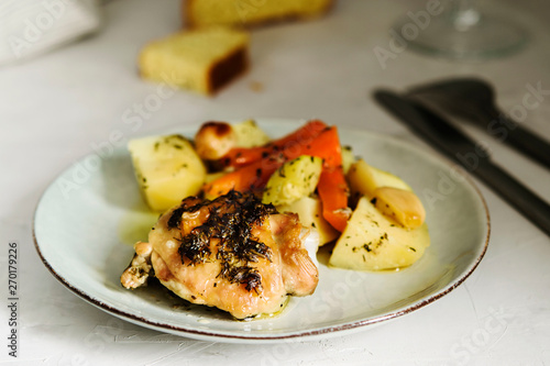 Homemade herb and spice chicken thighs baked with vegetables on a plate on grey background. Homemade lunch. Selective focus