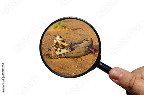 saddle for camel on the sand, view through a magnifying glass on a white background, magnifying glass in hand.