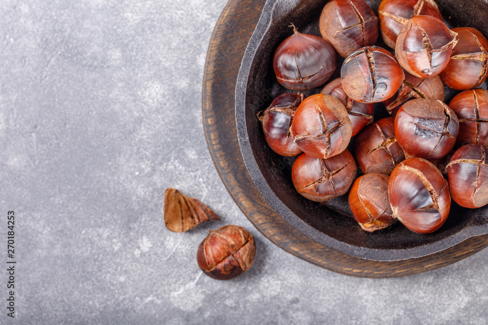 Obraz premium Roasted edible sweet chestnuts served in cast-iron skillet on gray background. Top view. Copy space.