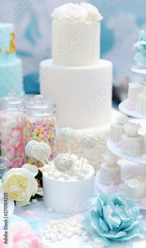 Traditional anniversary/wedding multi-layer cake decorated with flowers. And beautiful delicious sweet dessert - cupcakes, marshmallow, vanilla cake pops. Stylish sweet table.