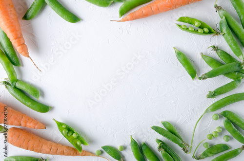 Fresh harvest of carrots and green peas in their pods on the white backgroud, top view.Frame made of tasty vegetables, empty space for design.Concept of healthy eating