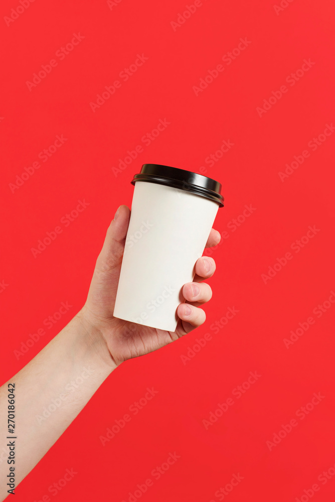 Paper cup of coffee or tea on a red background. Mockup of male hand holding paper cup isolated. Front view mockup of empty polystyrene coffee mug. Take away. Advertising coffee.