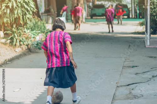 Back view of Girl student wear skirt to practice playing football alone on the street in the school.