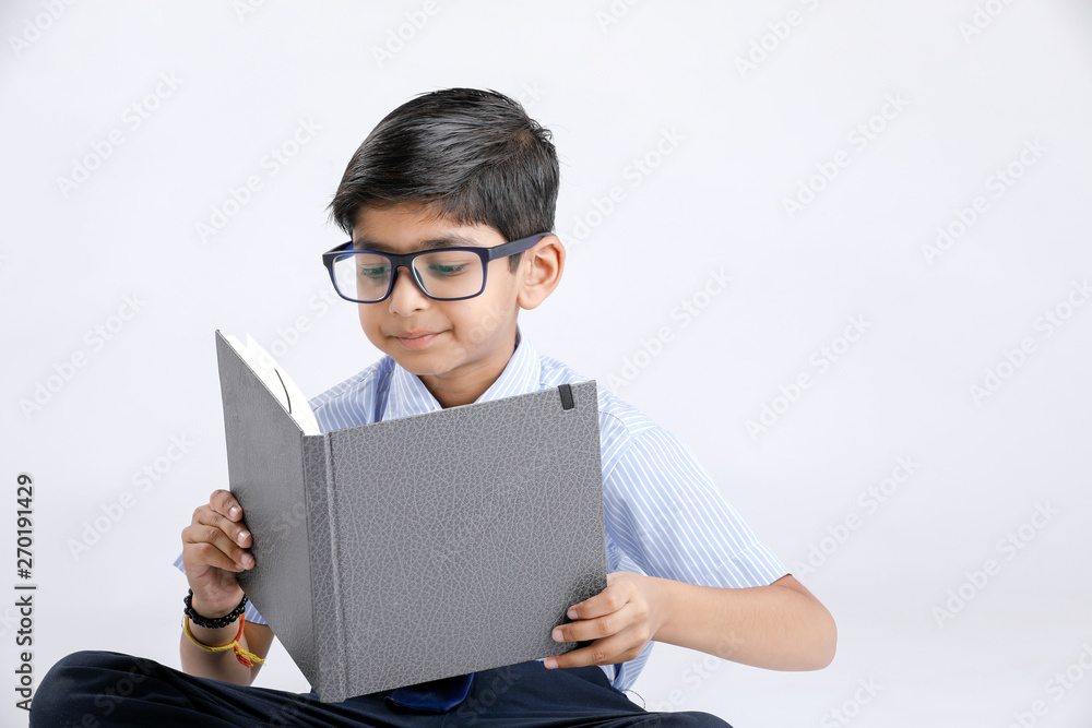 Cute little Indian/Asian school boy with spectacles reading book over white background Cute little Indian/Asian school boy with spectacles reading book over white background