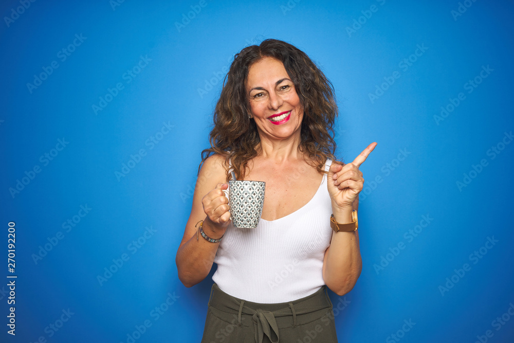 Obraz premium Middle age senior woman drinking a cup of coffee over blue isolated background very happy pointing with hand and finger to the side