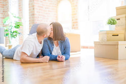 Young couple in love lying on the floor of new house arround cardboard boxes, smiling very happy for moving to a new apartment