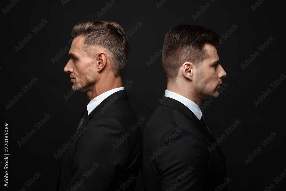 Handsome two adult business men posing isolated over black wall background. Handsome two adult business men posing isolated over black wall background.