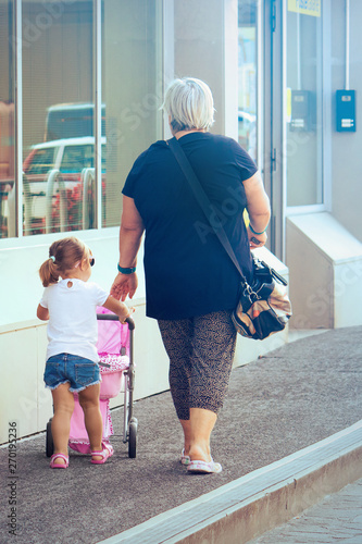 grandma walking with her granddaughter. The little girl plays with a pink stroller toy