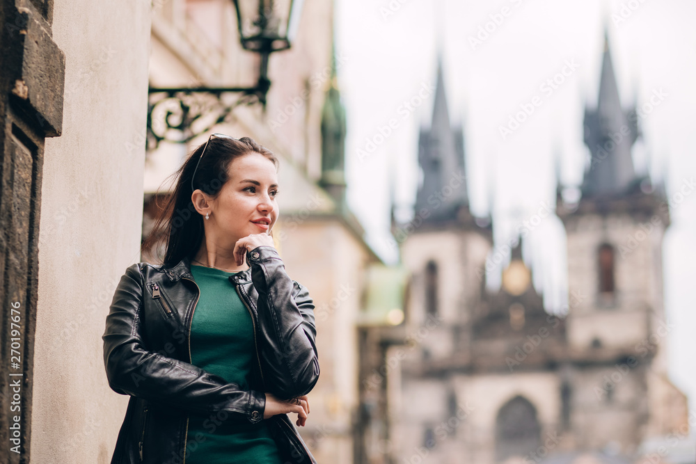 Fototapeta premium Street portrait of adorable brunette woman with long hair posing at Old Town Square in Prague. smiling pretty brunette girl, lifestyle. observatory of astronomical clock tower in Prague, Czech