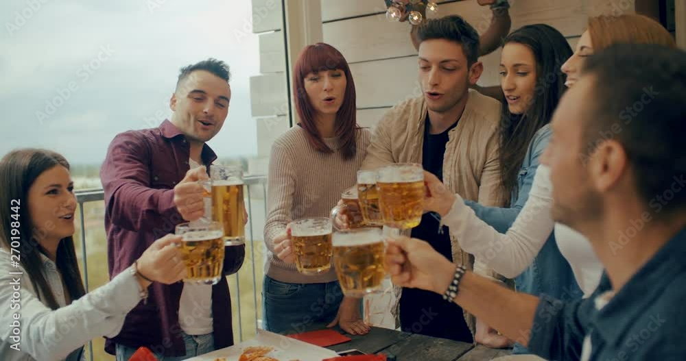 Millenial friends group drinking beer and sharing pizza slices on the rooftop at home - Friendship concept with young people having fun together eating snack at risto pub pizzeria. Shot in slow motion Millenial friends group drinking beer and sharing pizza slices on the rooftop at home - Friendship concept with young people having fun together eating snack at risto pub pizzeria. Shot in slow motion