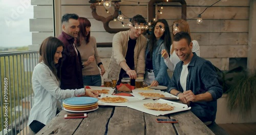 Millenial friends group drinking beer and sharing pizza slices on the rooftop at home - Friendship concept with young people having fun together eating snack at risto pub pizzeria. Shot in slow motion photo