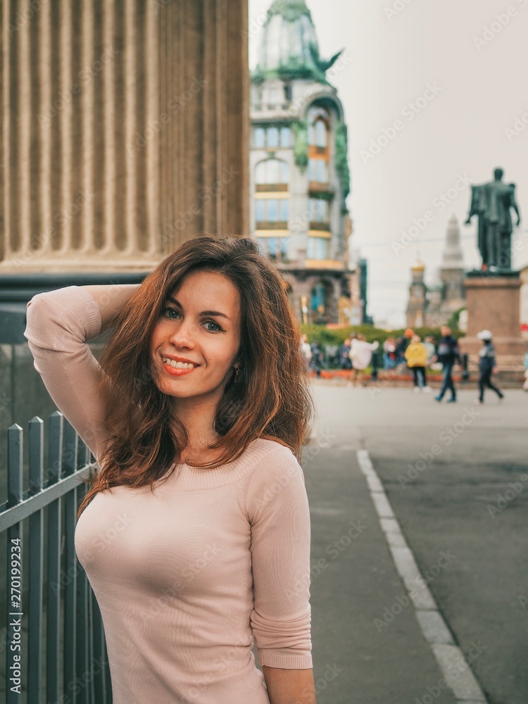 Fototapeta premium Brunette girl with long hair stands on the streets in the center of St. Petersburg near the canals on the background of the Kazan Cathedral