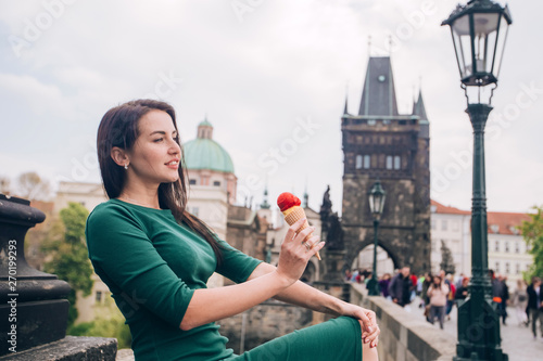 Молодая брюнетка женщина, сидя расслабленной и едят мороженое на стенах Карлова моста, над рекой Влтава, город Прага, в Чешской Республике.