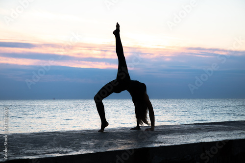 unrecognizable senoir woman with beautiful body profissiionally doing yoga at sunrise on the sea  silhouette of yoga poses
