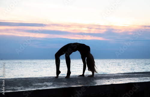 unrecognizable senoir woman with beautiful body profissiionally doing yoga at sunrise on the sea, silhouette of yoga poses