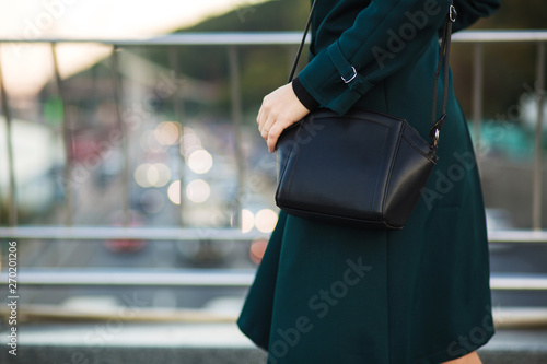 Trendy dressed woman holding leather purse at the background of bokeh. Copy space