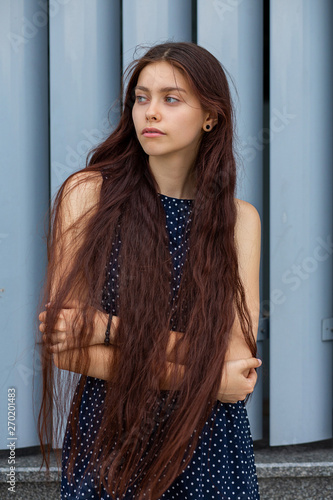 Fashionable long haired young lady posing near the metal shutters at the city