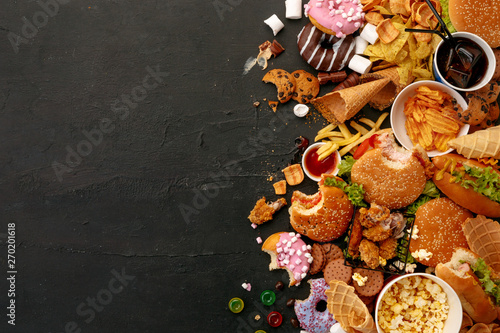 Fast food dish on black stone background. Take away unhealthy set including burgers, sauces, french fries, donuts, cola, sweets, icecream and biscuit. Diet temptation resulting in improper nutrition.
