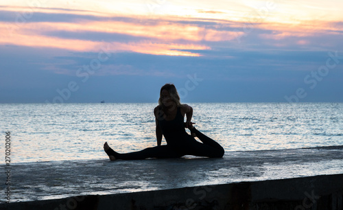 unrecognizable senoir woman with beautiful body doing yoga splits at sunrise on the sea, silhouette of yoga poses