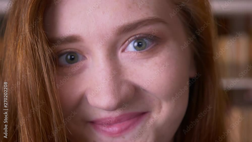 Closeup portrait of young cheerful redhead caucasian female student looking at camera smiling happily in the college library Closeup portrait of young cheerful redhead caucasian female student looking at camera smiling happily in the college library