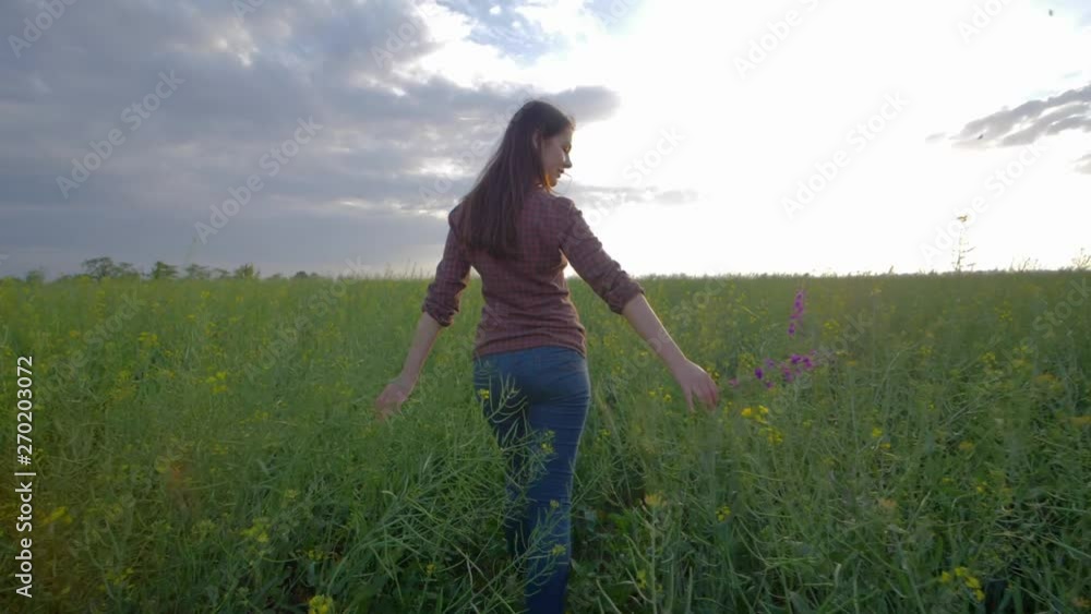 girl walking along a green rapeseed field and enjoying the beauty of nature on background of sky
