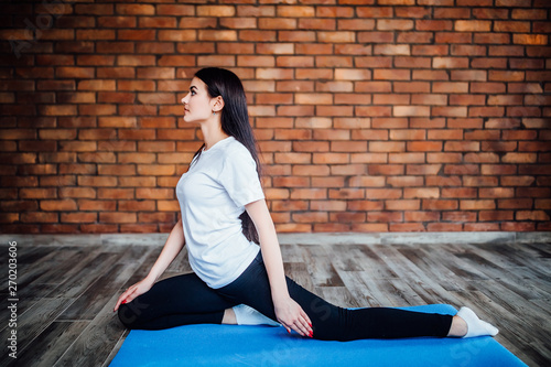 Slim brunette woman practices yoga in white backlit studio. Healthy life.