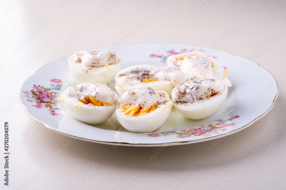 Sliced boiled eggs with mayonnaise and pepper in white plate isolated angle view Sliced boiled eggs with mayonnaise and pepper in white plate isolated angle view