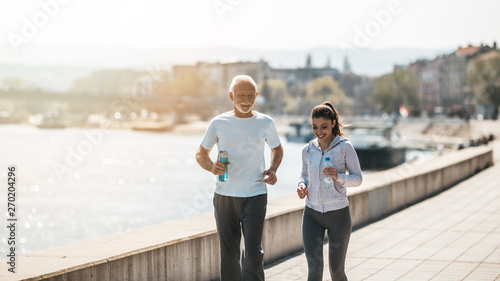 Fit senior man in good shape jogging and exercising together with his young adult daughter coach or instructor.